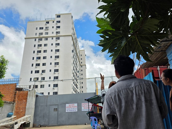 16日、カンボジアの住民が首都プノンペン郊外のセンソック地区にある「サクラ団地」のウェンチを見上げている。プノンペン＝イ・ヨングン記者。