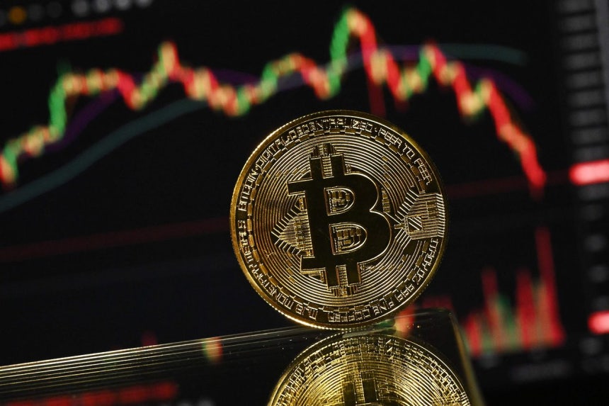 金メッキのビットコイン模型が、ビットコインの月間価格チャートが表示されたコンピューター画面の前で撮影された。［AFP＝聯合ニュース］