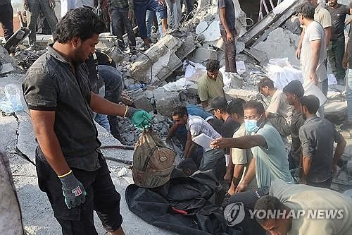 空爆で破壊されたイラン小学校残骸と救助隊員。ロイター＝聯合ニュース