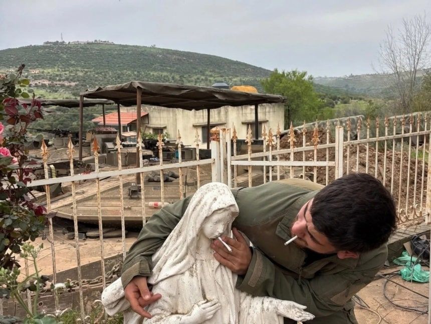   イスラエル軍服姿の男が聖母像の口元にたばこを近づける様子。［写真 SNS キャプチャー］