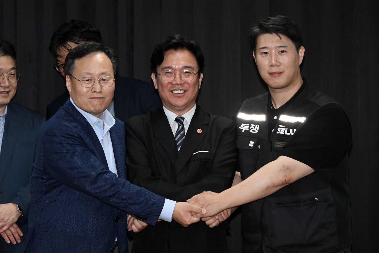 20日に京畿雇用労働庁で開かれたサムスン電子賃金交渉を終えた後、サムスン電子のヨ・ミョングDSピープルチーム長（左）と雇用労働部の金栄訓長官（中央）、サムスングループ超企業労働組合サムスン電子支部のチェ・スンホ委員長（右）が暫定合意案に署名した後手を取り合っている。［写真 ニュース1］