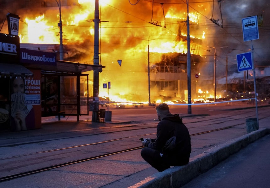 24日、ウクライナのキーウで発生したロシアのミサイルとドローン空爆現場に住民が座っている。［写真 ロイター＝聯合ニュース］