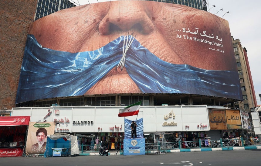 先月28日、イラン・テヘランの広場の広告板に、ドナルド・トランプ米大統領の口をホルムズ海峡を象徴する青い布と糸、針で縫い付けた絵が掲示されている。EPA＝聯合ニュース