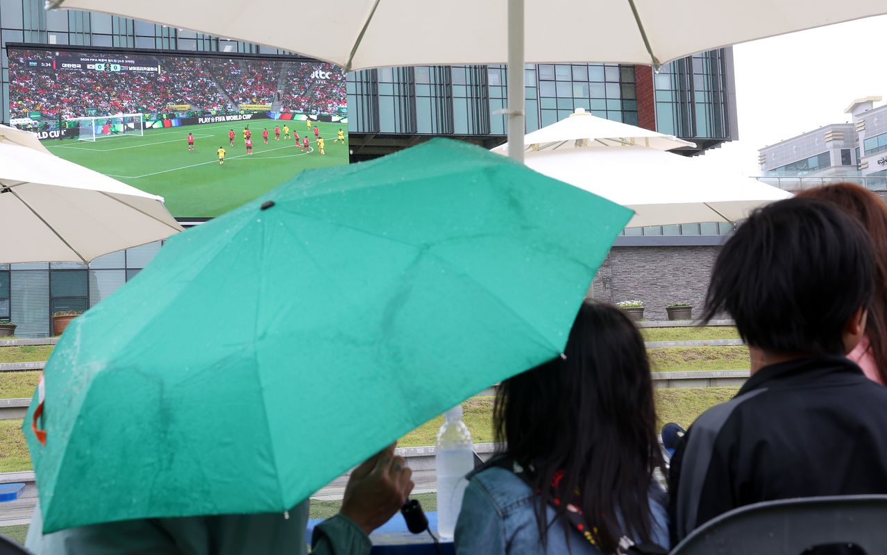 2026年FIFAワールドカップ北中米大会のグループA第3戦、韓国対南アフリカ戦が行われた25日、春川（チュンチョン）市庁前広場で、傘を差した市民たちが大型スクリーンで試合を観戦している。聯合ニュース
