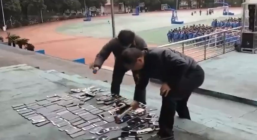   学生から押収した携帯電話をハンマーで破壊している教師ら。［X キャプチャー］