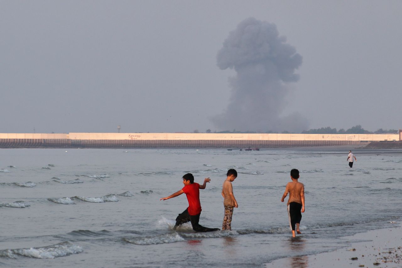   ホルムズ海峡沿岸で遊ぶ少年たちの背後に、米軍の空爆による黒煙が立ち上っている。AP＝聯合ニュース