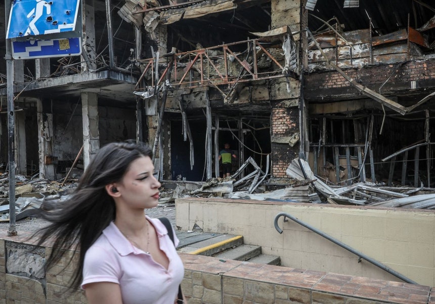 5月、ウクライナのキーウで女性がロシアのミサイル攻撃で破壊された建物のそばを歩いている。［写真 ロイター＝聯合ニュース］