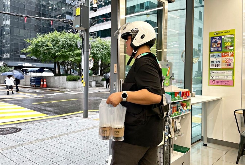 コンビニエンスストア「CU」で、配達員がコーヒーを受け取り、配達の準備をしている。［写真 CU］