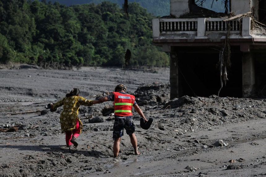 28日（現地時間）、ネパールのヌワコット地域のトリシュリで鉄砲水と土砂崩れが発生した後、救助隊員が泥に覆われた道路を通っていた女性を助けている。ロイター＝聯合ニュース