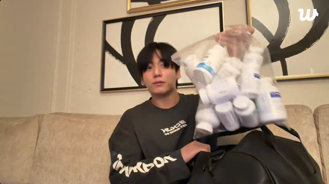  数十個の薬の容器が入った袋を持ち上げて見せるBTSのJUNG KOOK。［写真 Weverse キャプチャー］