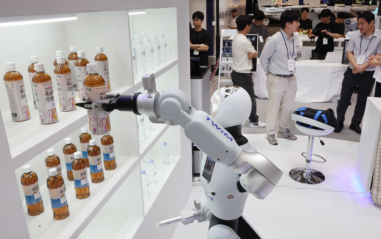釜山市海雲台区（プサンシ・ヘウンデグ）のBEXCO第1展示場で開かれた「2026ワールドスマートシティエキスポ」のスマートシティ釜山ブースで、参加者に渡す飲料のペットボトルをつかむAI搭載の人型サービスロボット。［聯合ニュース］