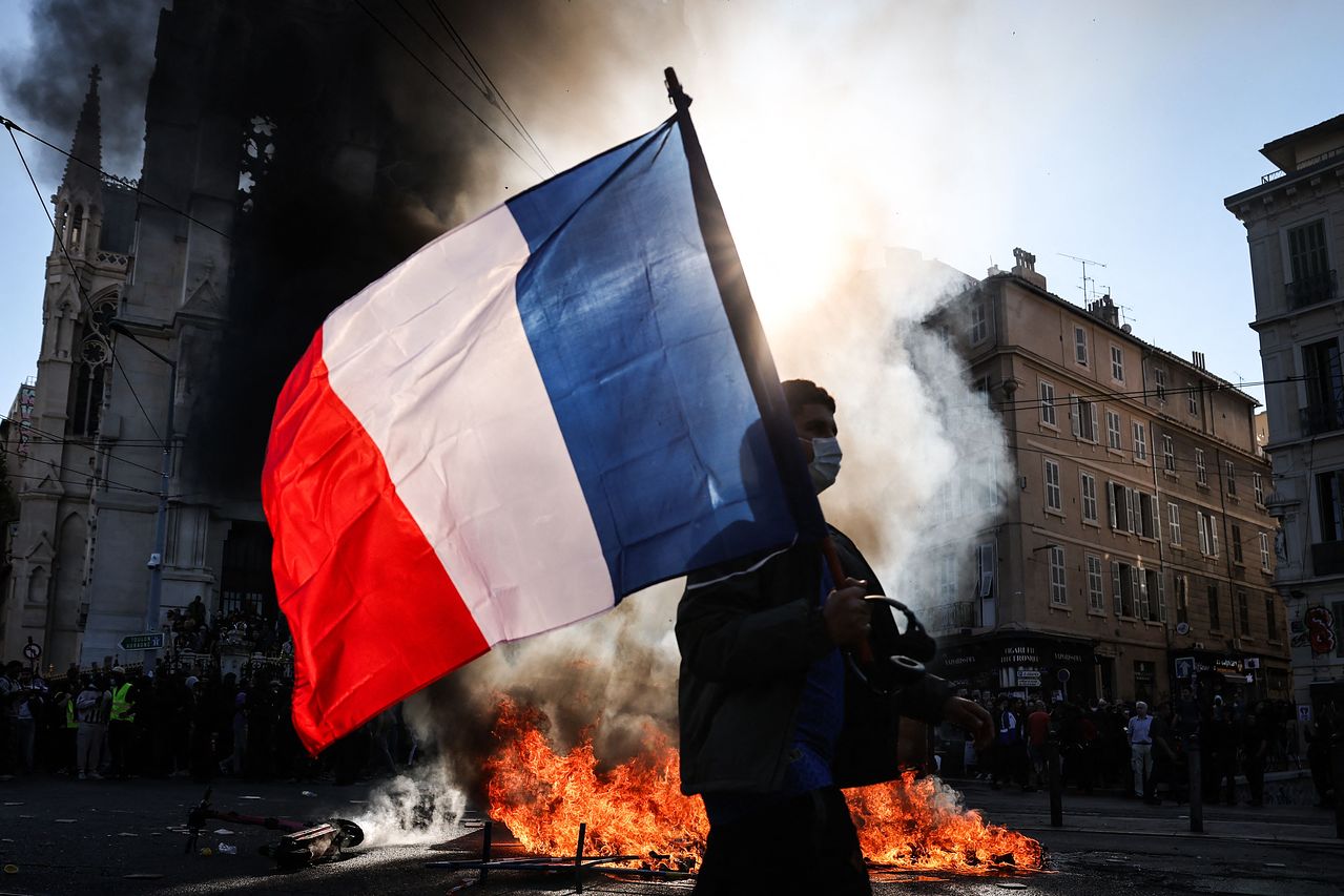 17日（現地時間）、フランス南部マルセイユで「高い生活費」に抗議するデモが始まる前に発生した衝突の現場で、デモに参加した市民がフランス国旗を振りながら炎のそばを通り過ぎている。学生が始めたデモは生活費など幅広い分野に拡大しており、フランス当局はデモに20万人以上が参加していると明らかにした。AFP＝聯合ニュース