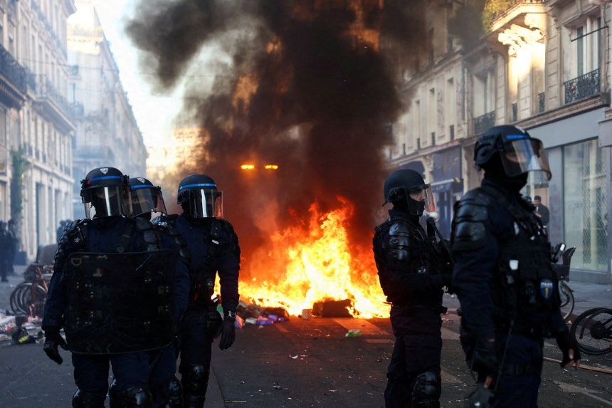 18日（現地時間）、仏パリで物価や原油価格の上昇に抗議する全国規模デモの翌日、鎮圧装備を身に着けた警察官らが炎のそばを警戒している。［ロイター＝聯合ニュース］
